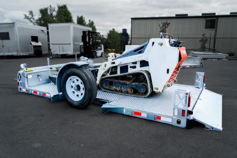 Good flatbed trailer, lowered to the ground, Bobcat loaded, ramp down.