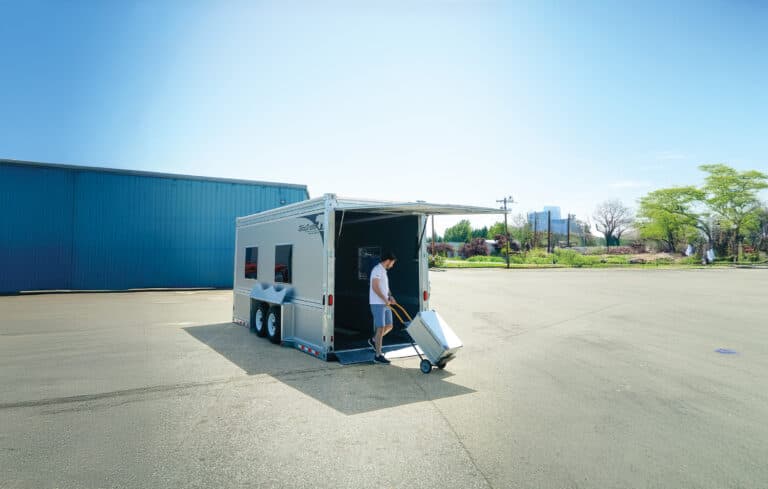 A man loading cargo into a GT-HDX, using the fold-down ramp. Trailer is lowered, flush to the ground.