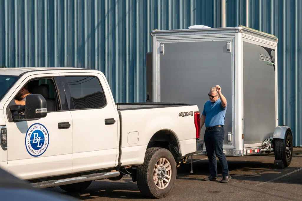 Drop deck trailer maintenance is easy when you roll out with a Good Trailer. A man signals a driver when he starts to haul a '9 enclosed Good Trailer.