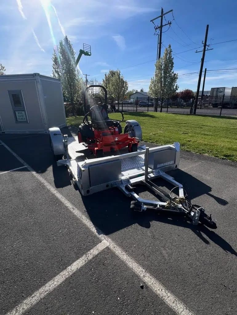 Equipment rental yard trailers - zero turn mower on 13' flatbed plus Good Modular Structure in the background.