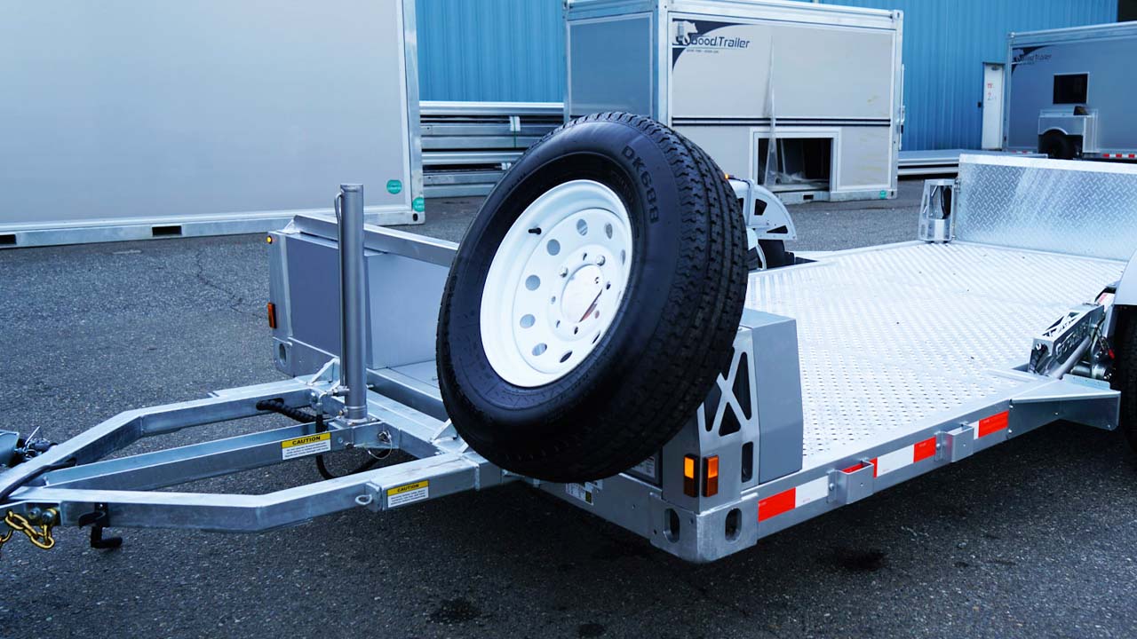 Spare tire attached to front of flatbed trailer.